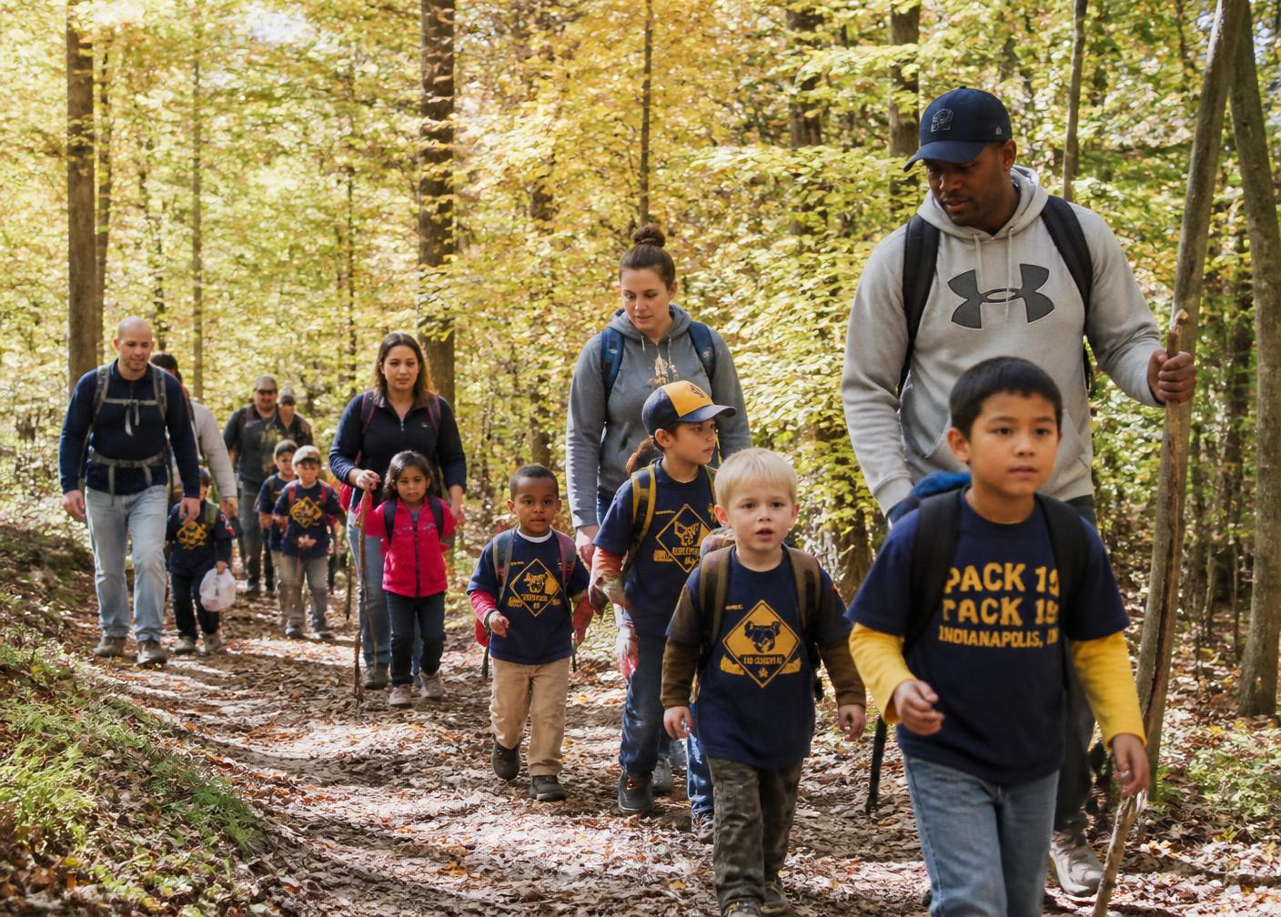 Cub Scouts hiking a wooded trail beside a creek with their leader