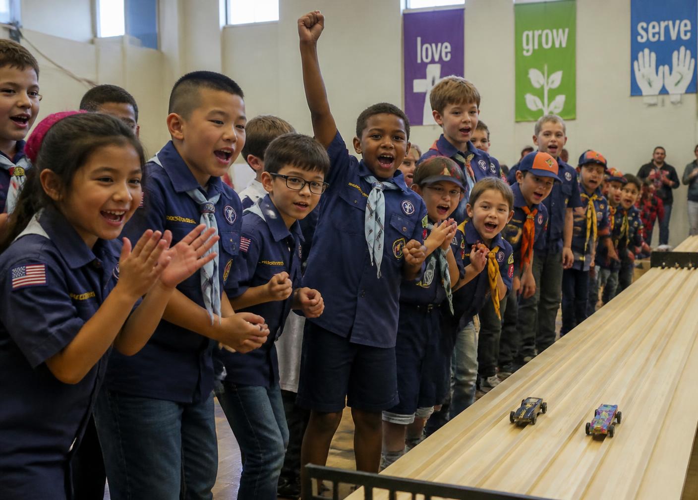 Cub Scouts kneeling beside a pinewood derby track as their cars race